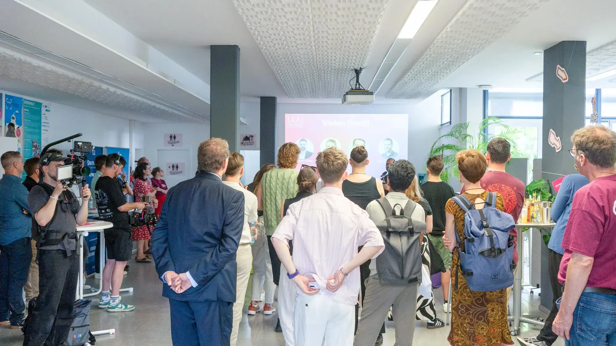 Dieses Foto zeigt Besucher eines Events von hinten, die auf eine Bühne schauen und einer Präsentation zuhören.
