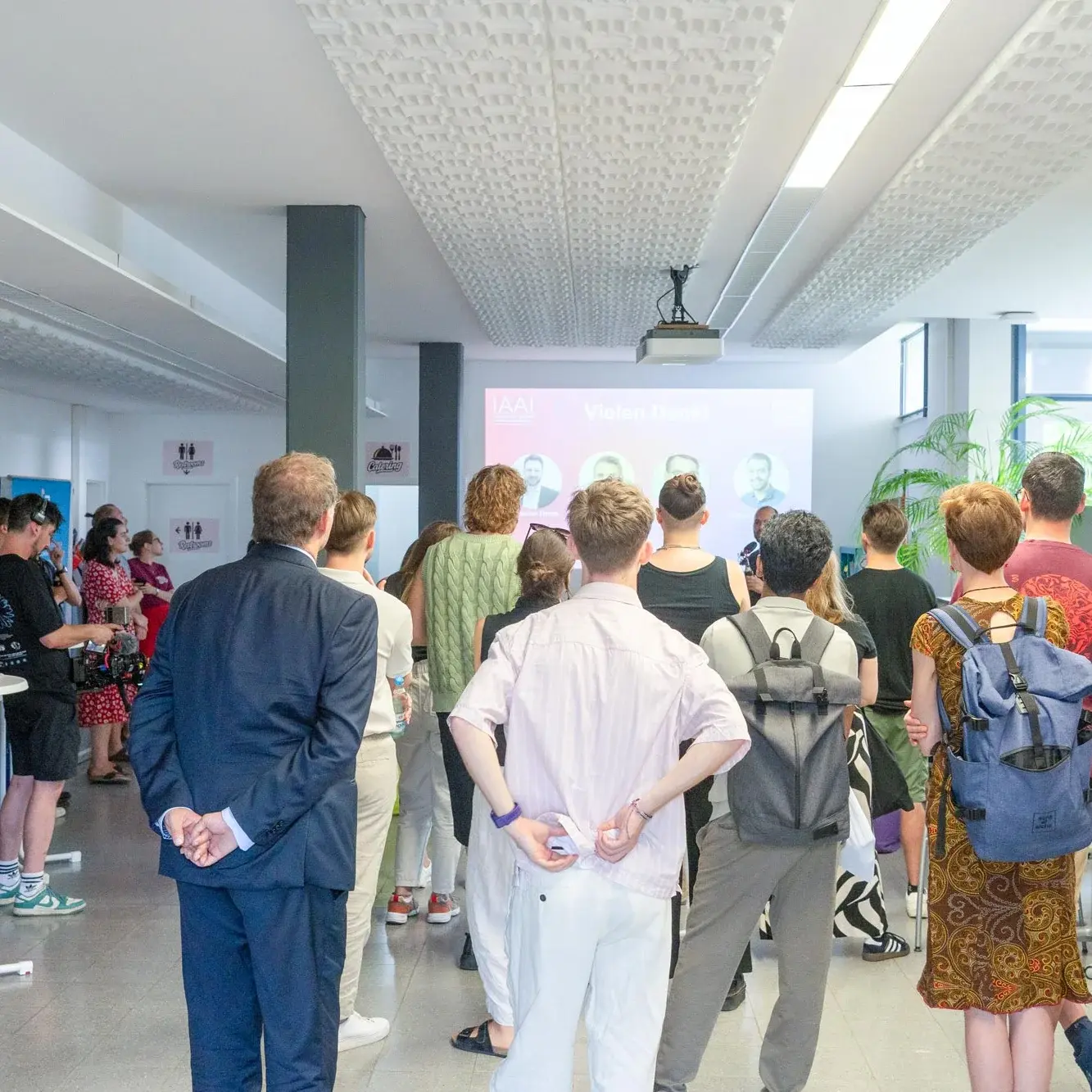 Dieses Foto zeigt Besucher eines Events von hinten, die auf eine Bühne schauen und einer Präsentation zuhören.