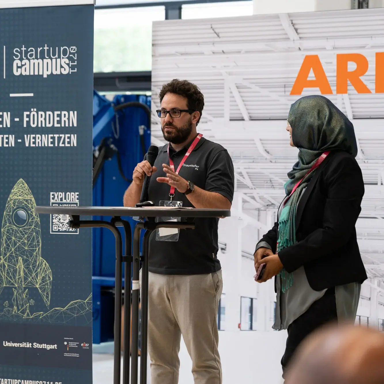 Eine Gründerin und ein Gründer stehen auf einer Startup Bühne und diskutieren im Rahmen einer Panel-Diskussion